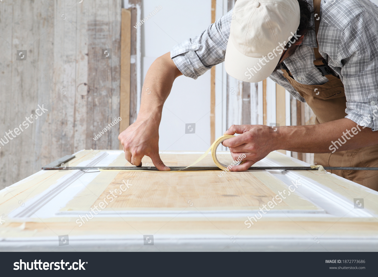 stock-photo-male-carpenter-working-the-wood-in-carpentry-workshop-putting-paper-masking-tape-on-wooden-door-1872773686